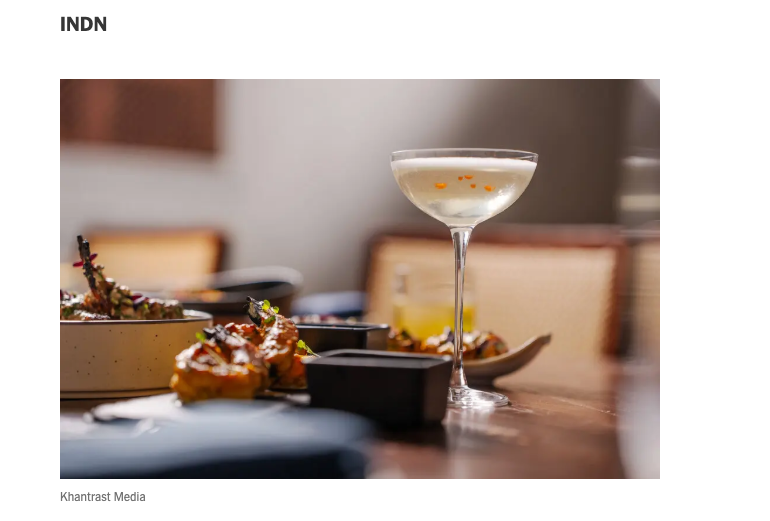 Published INDN photograph of a cocktail and dishes, with the Khantrast Media photography credit visible beneath it.